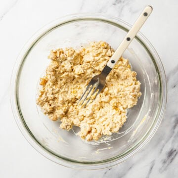 Fork mashing chickpea salad in glass bowl.