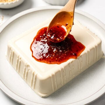 Spooning chili crisp sauce over silken tofu.