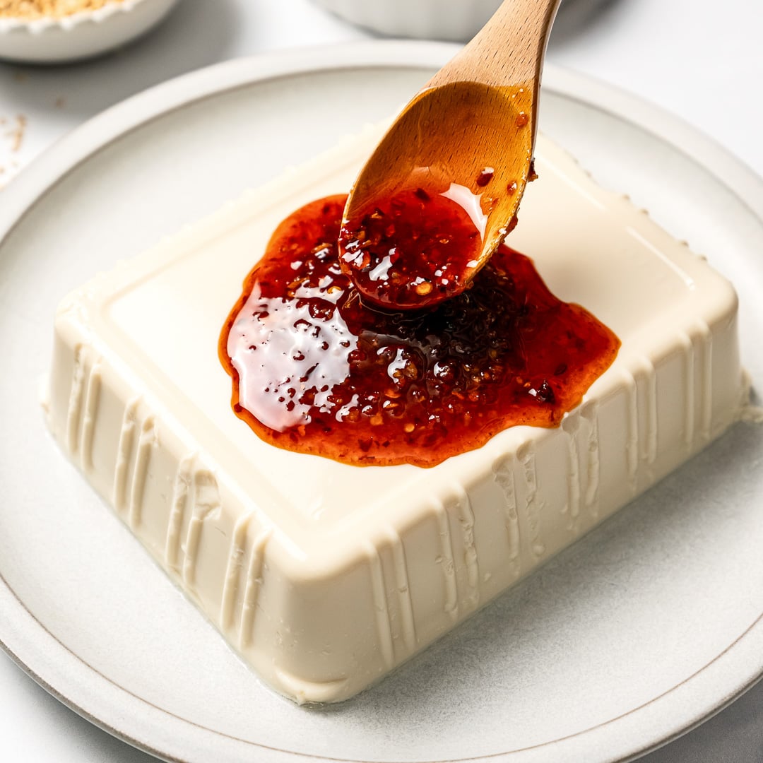 Spooning chili crisp sauce over silken tofu.