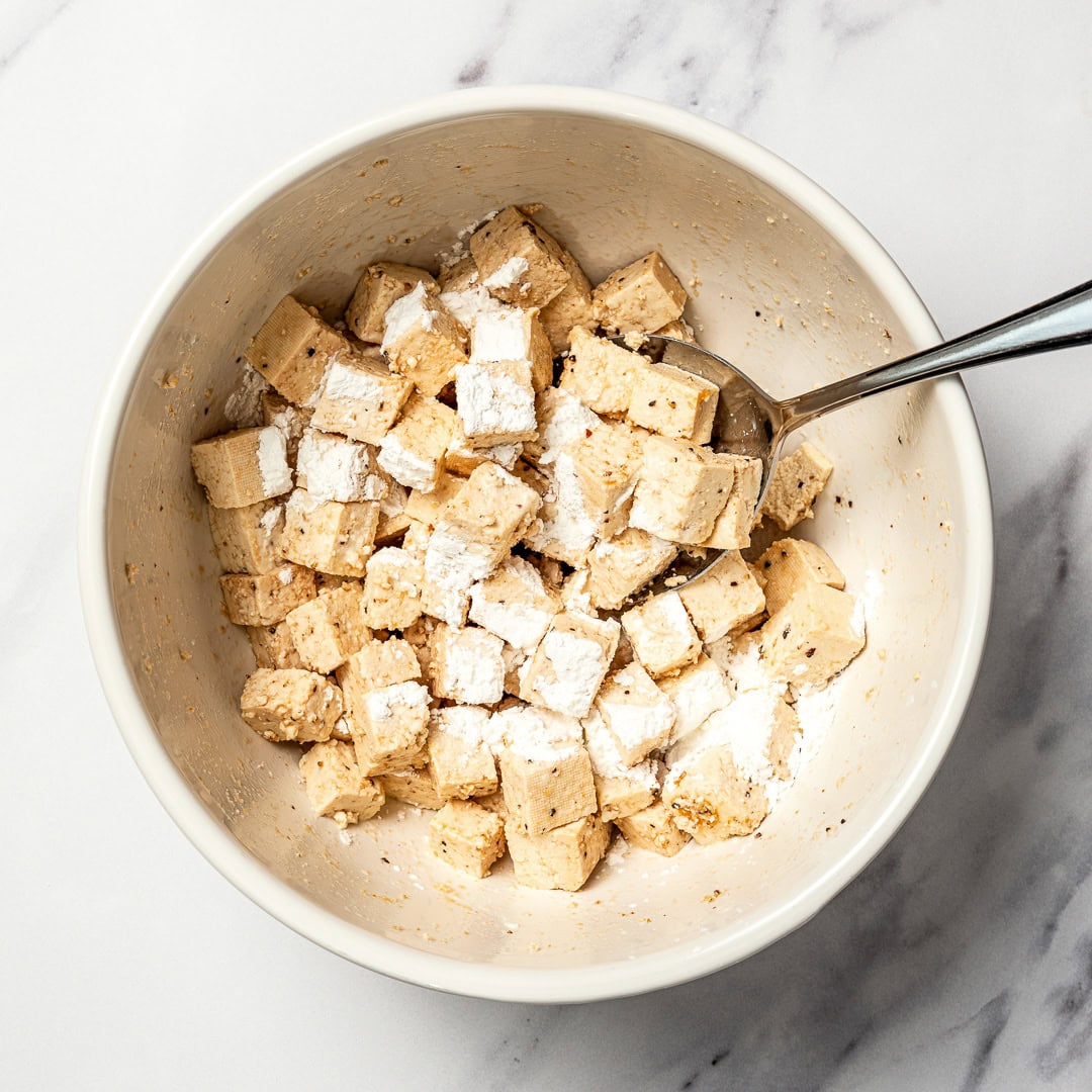Whether you pan-fry, bake, or use an air fryer, this easy crispy tofu recipe turns out golden, flavorful, and delicious every single time! Cornstarch sprinkled onto bowl of tofu.