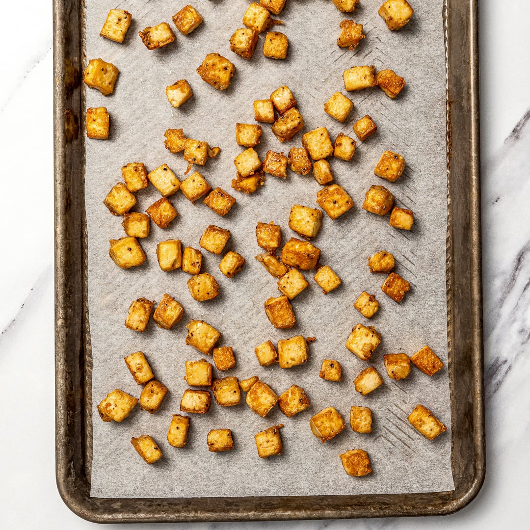Whether you pan-fry, bake, or use an air fryer, this easy crispy tofu recipe turns out golden, flavorful, and delicious every single time! Crispy tofu on parchment-lined pan.