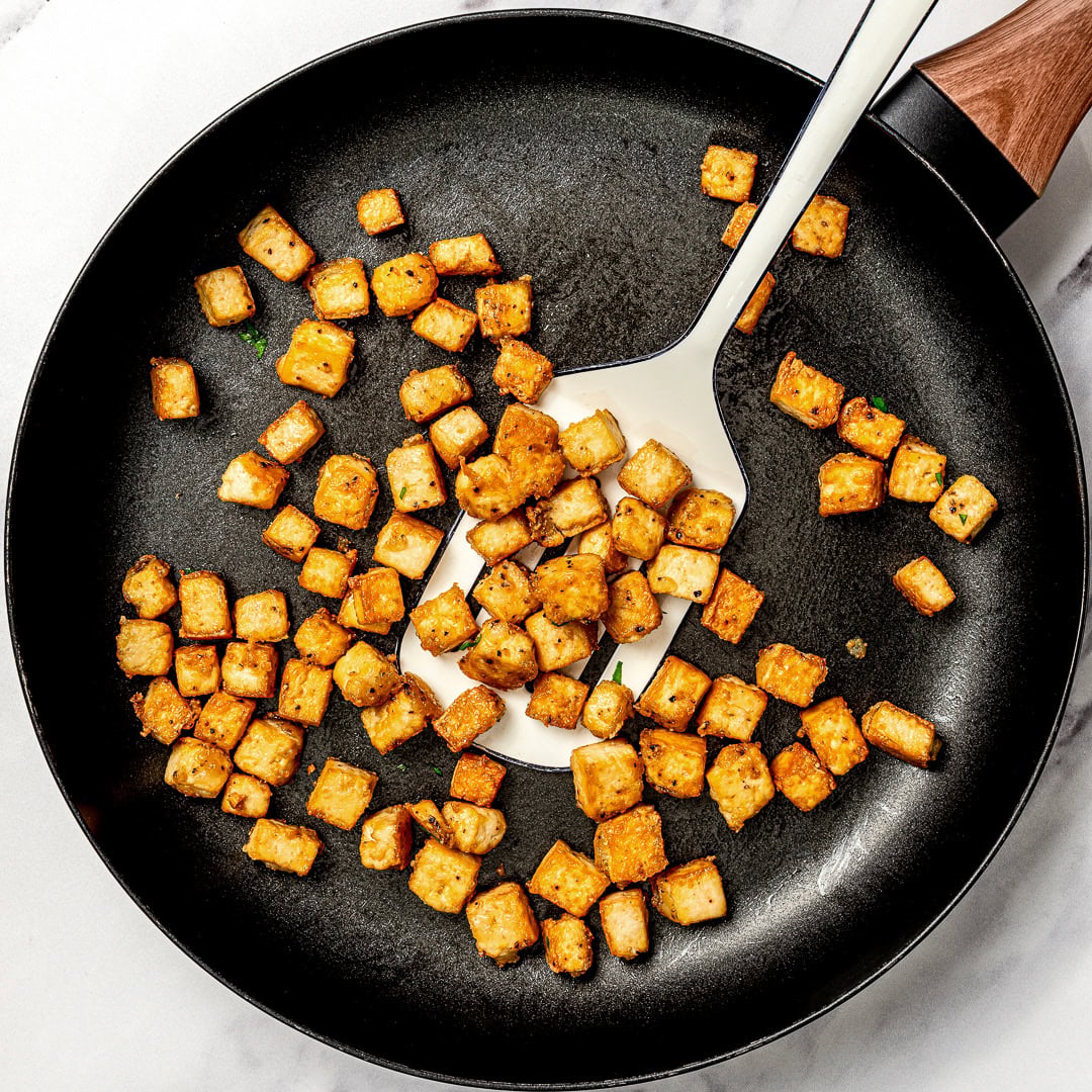 Whether you pan-fry, bake, or use an air fryer, this easy crispy tofu recipe turns out golden, flavorful, and delicious every single time! Spatula in pan with crispy tofu.