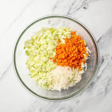 Chopped carrots, onion, and cabbage in glass bowl.