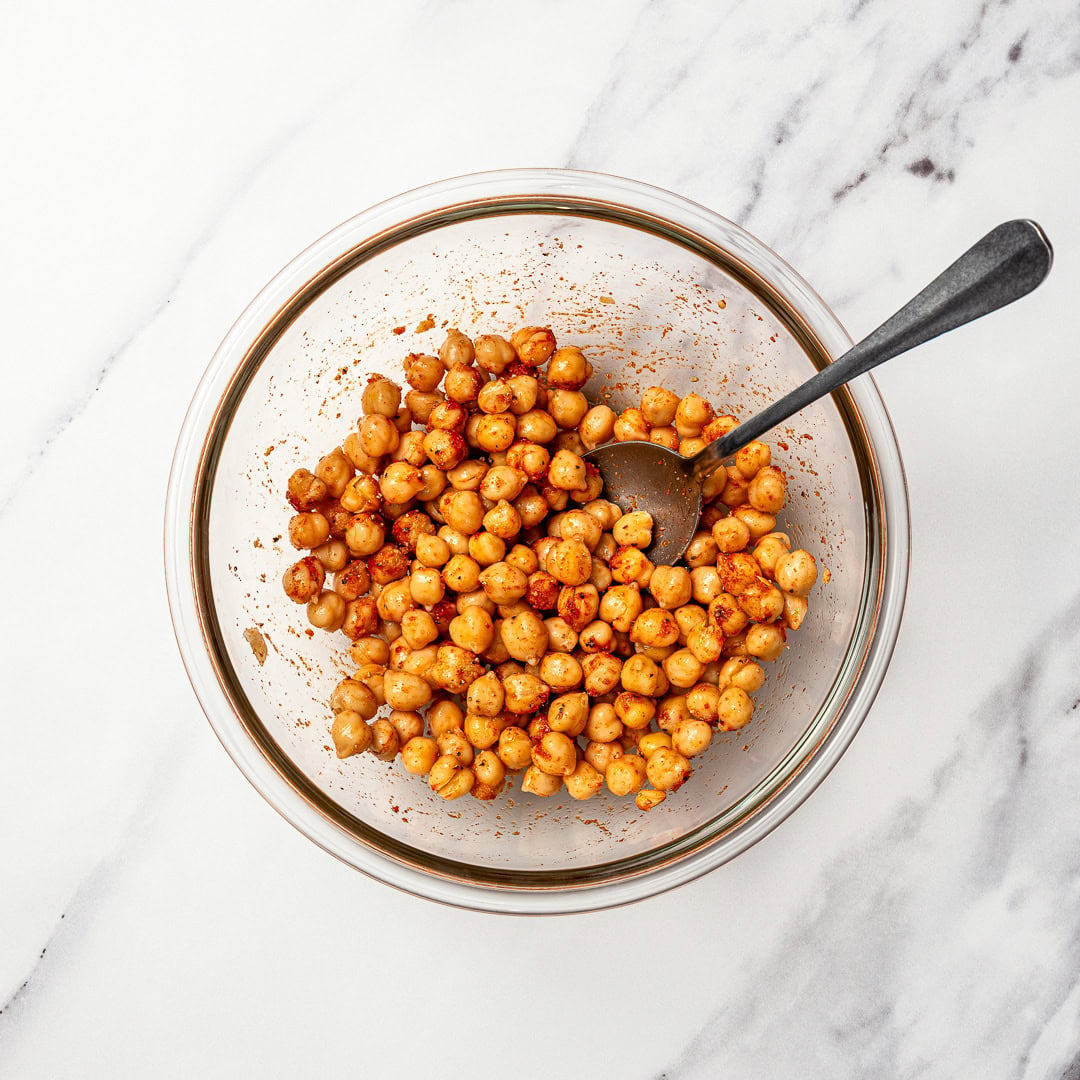 Made with simple ingredients in just 10 minutes, this crunchy hummus veggie wrap is perfect for lunch, meal prep, or an easy no-cook dinner! Seasoned chickpeas in bowl with spoon.