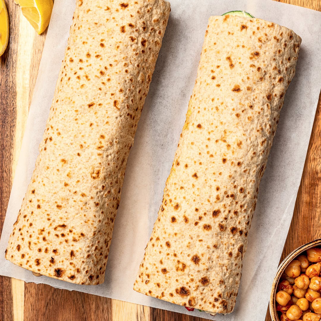 Made with simple ingredients in just 10 minutes, this crunchy hummus veggie wrap is perfect for lunch, meal prep, or an easy no-cook dinner! Two veggie wraps on parchment paper.