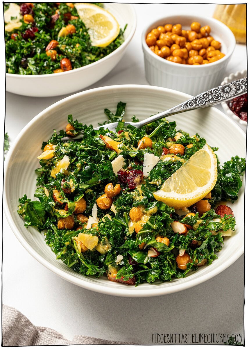 With shredded kale, zippy lemon dressing, dried cranberries, almonds and crispy chickpeas, this easy kale salad recipe is the best ever! Bowl of kale salad with lemon wedge and fork.