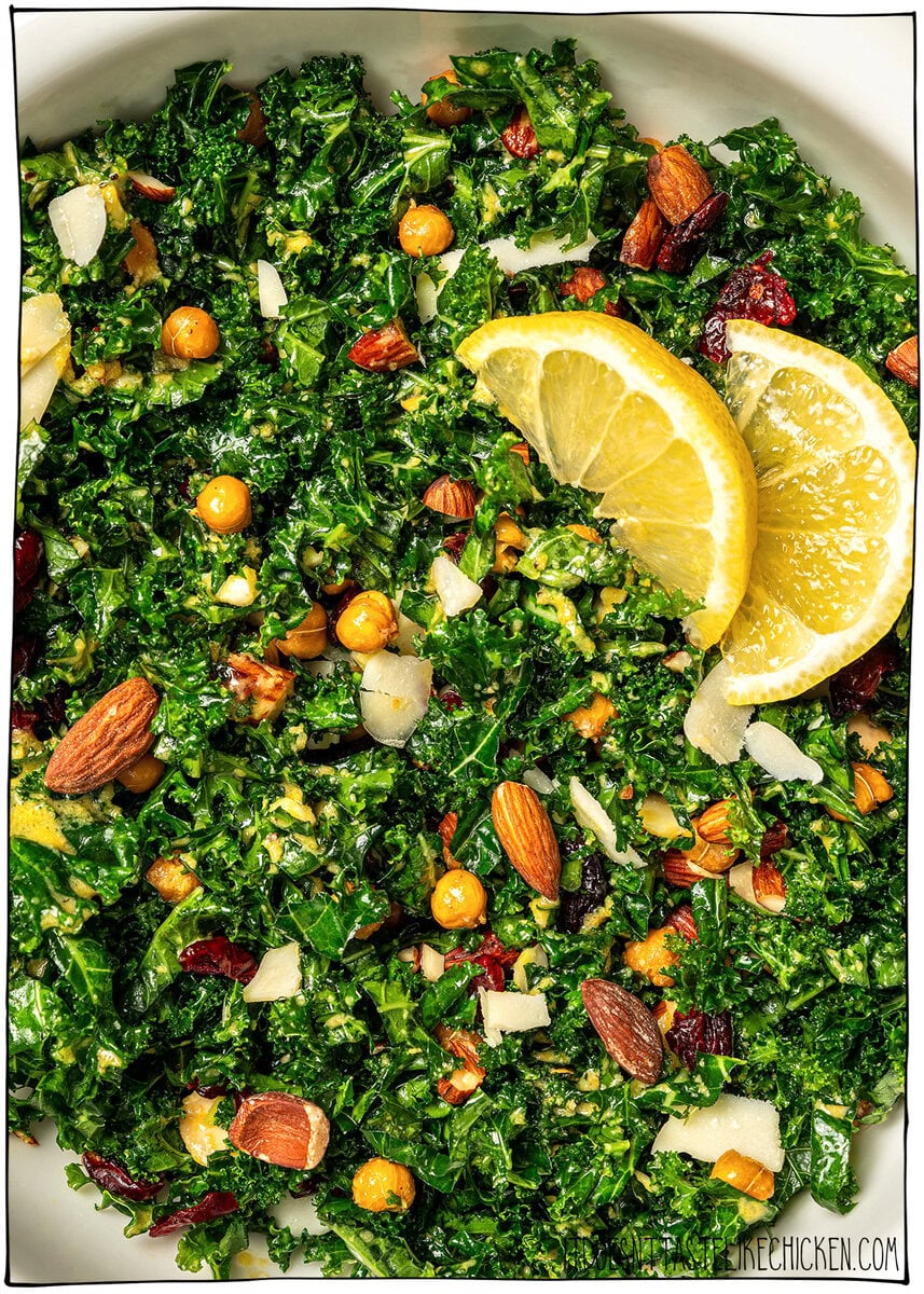 With shredded kale, zippy lemon dressing, dried cranberries, almonds and crispy chickpeas, this easy kale salad recipe is the best ever! Kale salad in bowl with two slices of lemon.