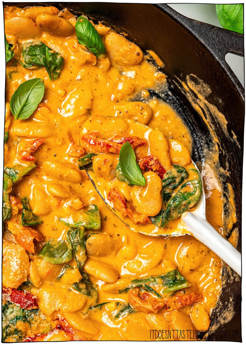 Marry me butter beans are an easy one-pan vegan dinner recipe with a creamy sun-dried tomato garlic sauce that tastes restaurant-worthy! Spoonful of marry me butter beans in pan.