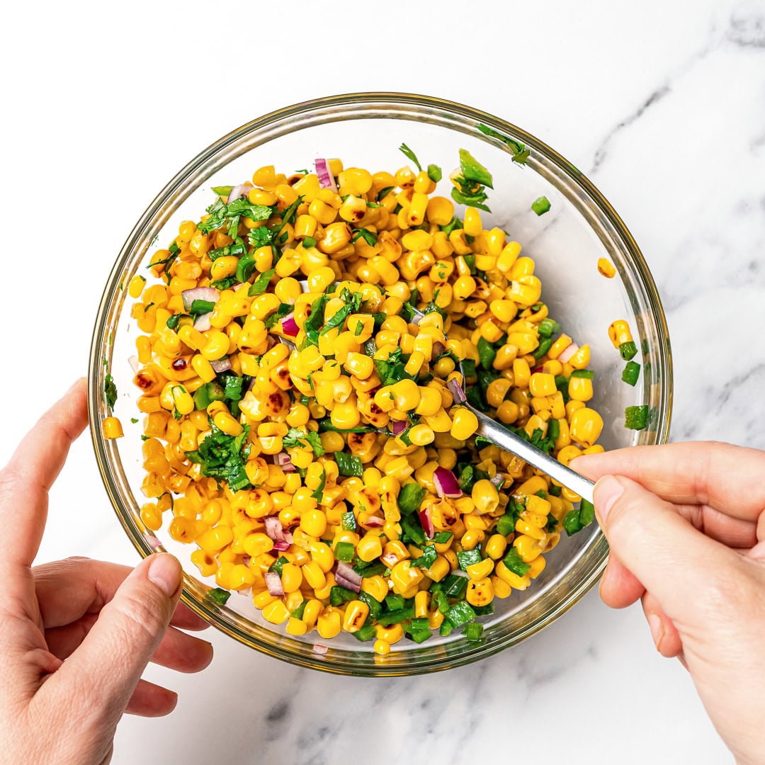 Made with charred corn, roasted poblano, cilantro, lime and red onion, this copycat Chipotle corn salsa is bright, smoky and so delicious! Stirring corn salsa in bowl.