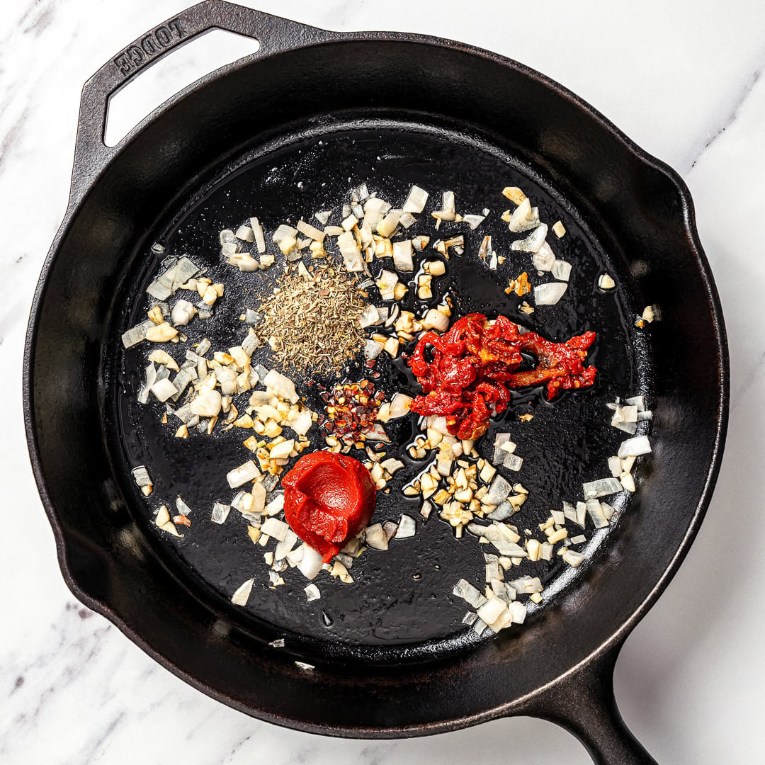 Marry me butter beans are an easy one-pan vegan dinner recipe with a creamy sun-dried tomato garlic sauce that tastes restaurant-worthy! Onions, seasonings, sun-dried tomatoes, and tomato paste in skillet.