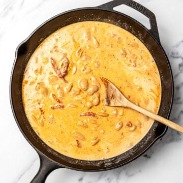 Wooden spoon in skillet of marry me butter beans.