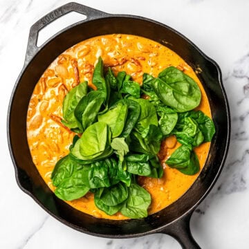 Baby spinach leaves added to skillet of marry me butter beans.