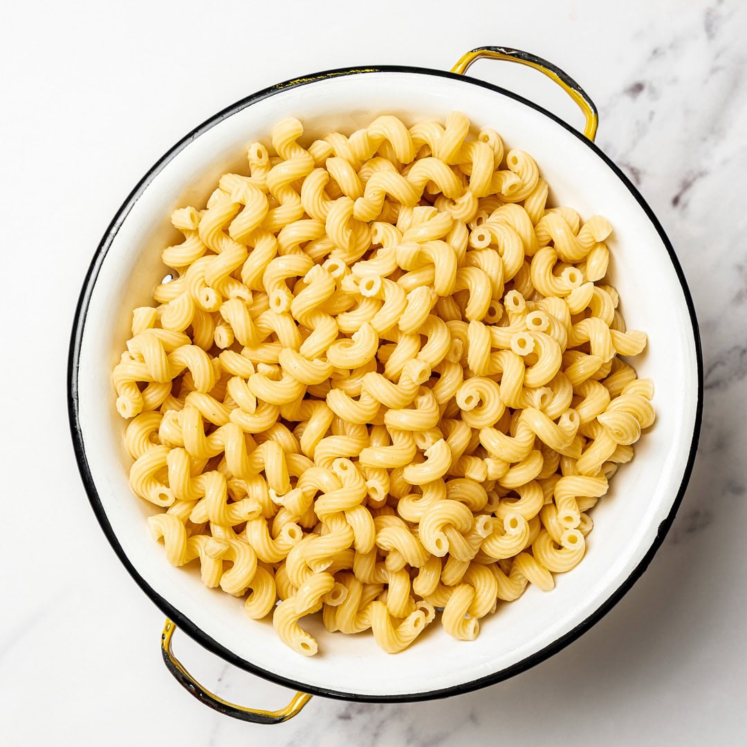 Bowl of pasta salad with text overlay that reads Mediterranean chickpea pasta salad. Cooked pasta in colander.