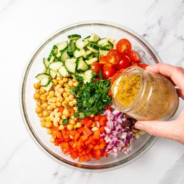 Pouring dressing into bowl of vegetables and chickpeas.
