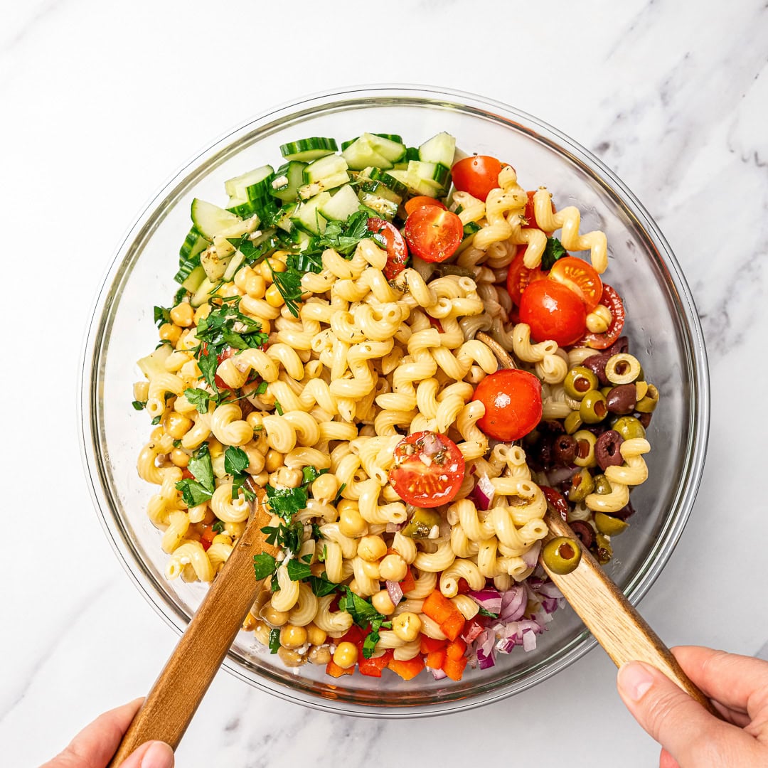 Bowl of pasta salad with text overlay that reads Mediterranean chickpea pasta salad. Tossing Mediterranean chickpea pasta salad in bowl.
