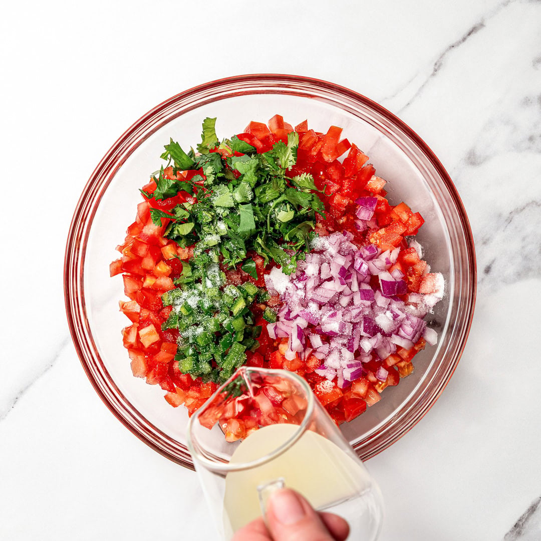 This pico de gallo tastes just like Chipotle's, but even better because it's extra fresh, easy to customize, and made at home in minutes! Pouring lime juice into bowl of pico de gallo ingredients.