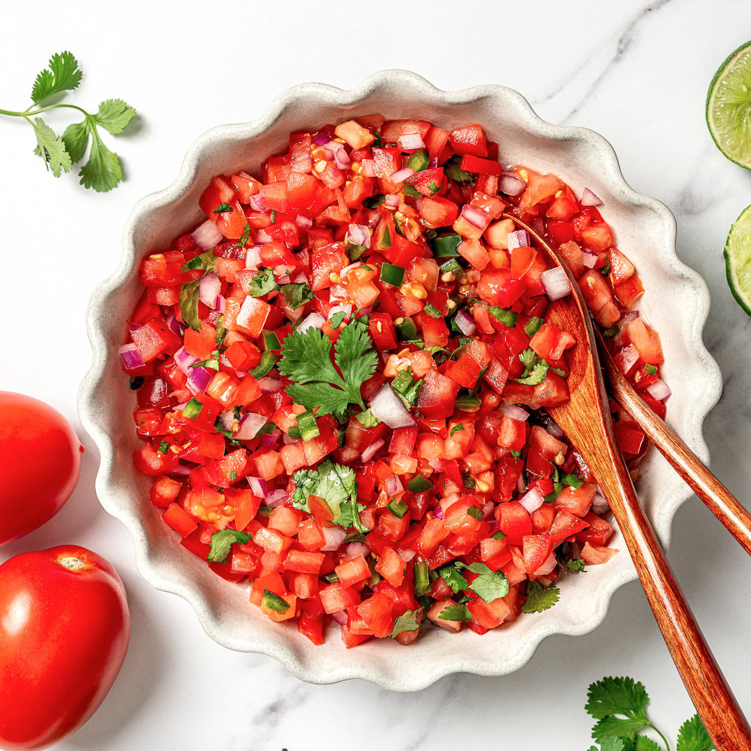 This pico de gallo tastes just like Chipotle's, but even better because it's extra fresh, easy to customize, and made at home in minutes! Bowl of pico de gallo with two wooden spoons.