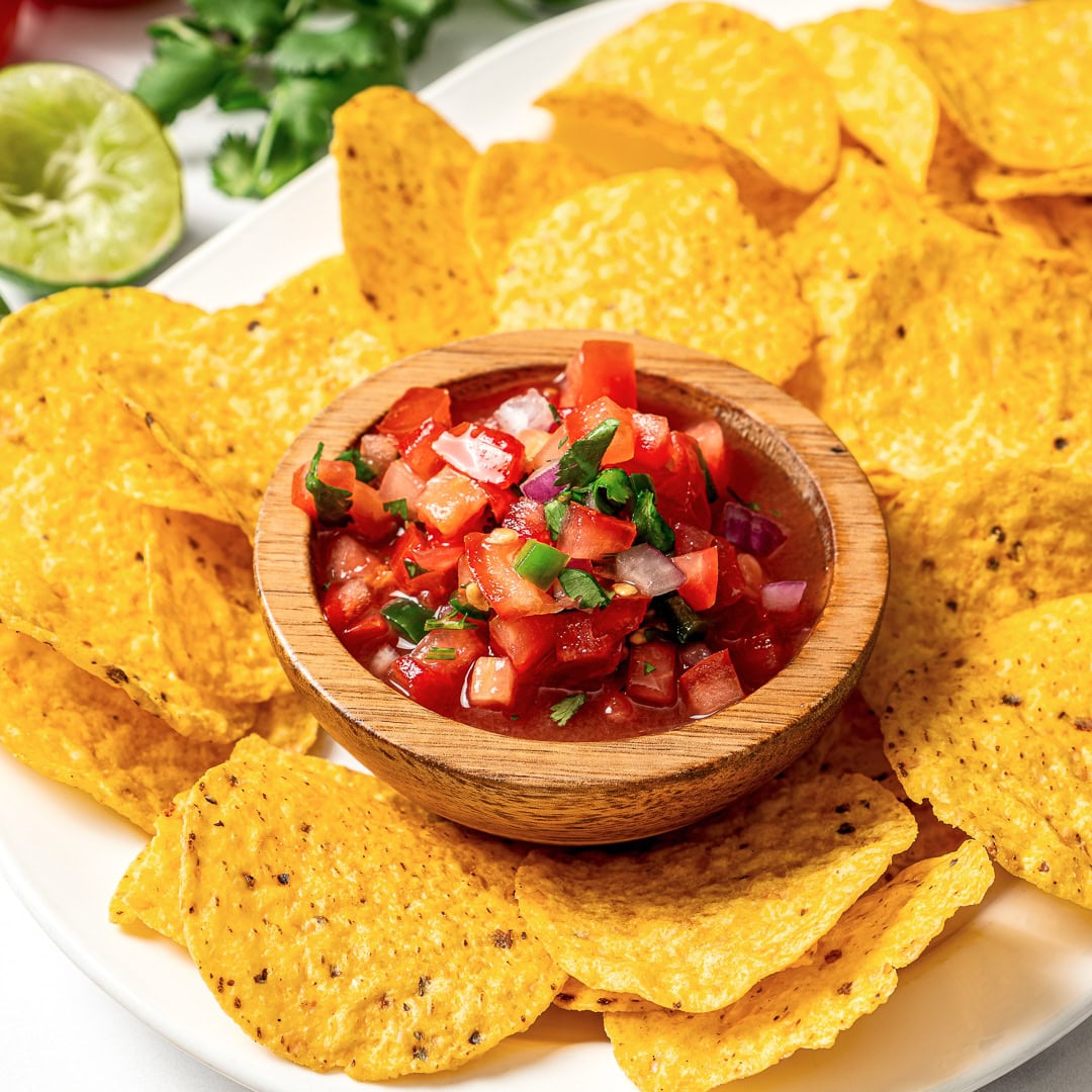 This pico de gallo tastes just like Chipotle's, but even better because it's extra fresh, easy to customize, and made at home in minutes! Bowl of pico de gallo on platter with tortilla chips.