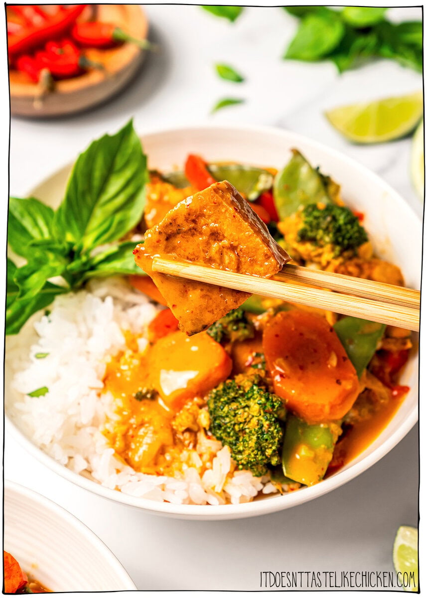 This easy vegan Thai red curry is creamy, cozy and packed with tender veggies and tofu in a rich coconut curry sauce. Perfect for busy days! Chopsticks holding cube of tofu over bowl of vegan Thai red curry.