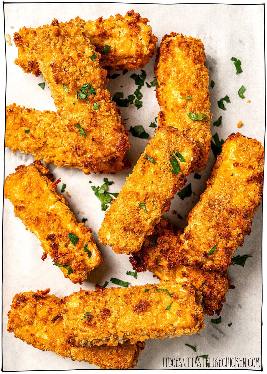 Plate of tofu chicken with sauce, with text overlay that reads vegan chicken fingers. Crispy tofu chicken fingers piled onto parchment paper.