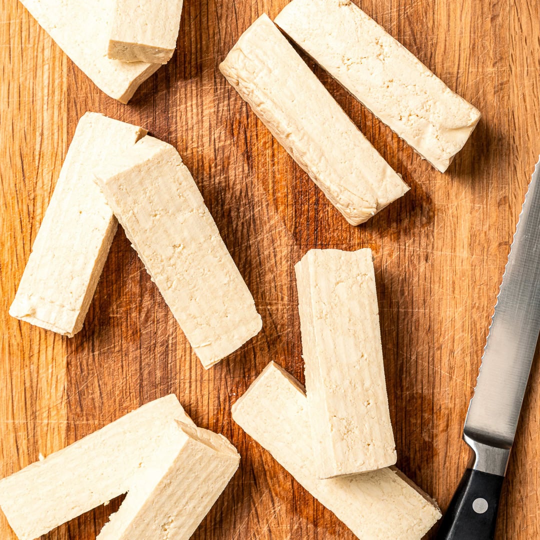 Plate of tofu chicken with sauce, with text overlay that reads vegan chicken fingers. Tofu cut into strips on wooden board.