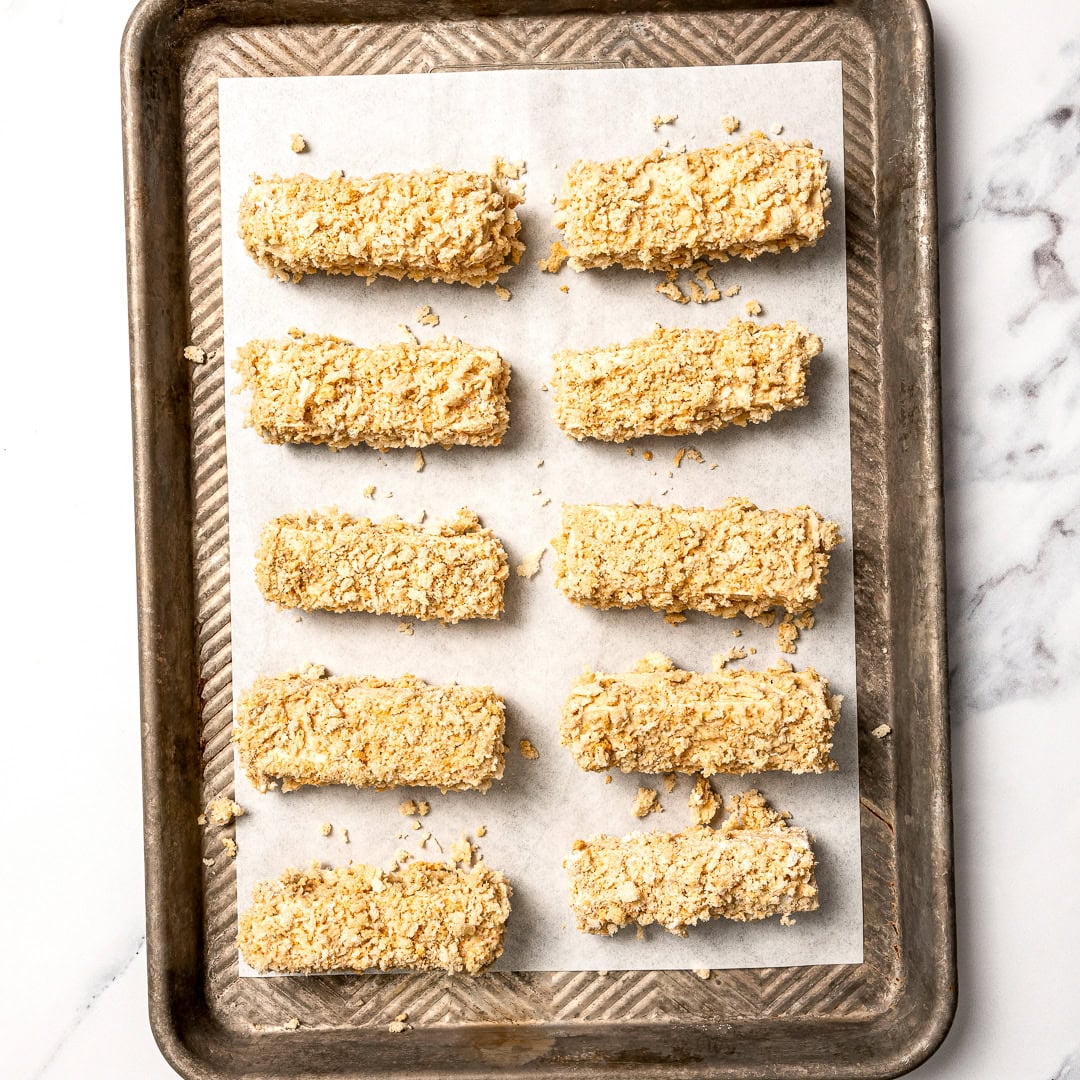 Plate of tofu chicken with sauce, with text overlay that reads vegan chicken fingers. Tofu chicken fingers on parchment lined pan before baking.