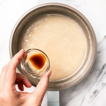 Pouring vanilla into vegan sweetened condensed milk in pan.