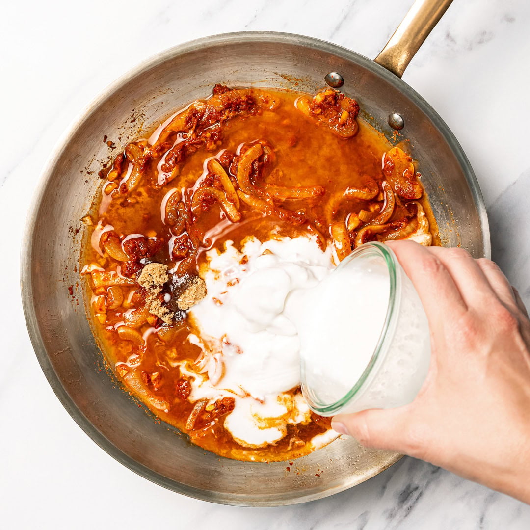 This easy vegan Thai red curry is creamy, cozy and packed with tender veggies and tofu in a rich coconut curry sauce. Perfect for busy days! Pouring coconut milk into pan for curry.