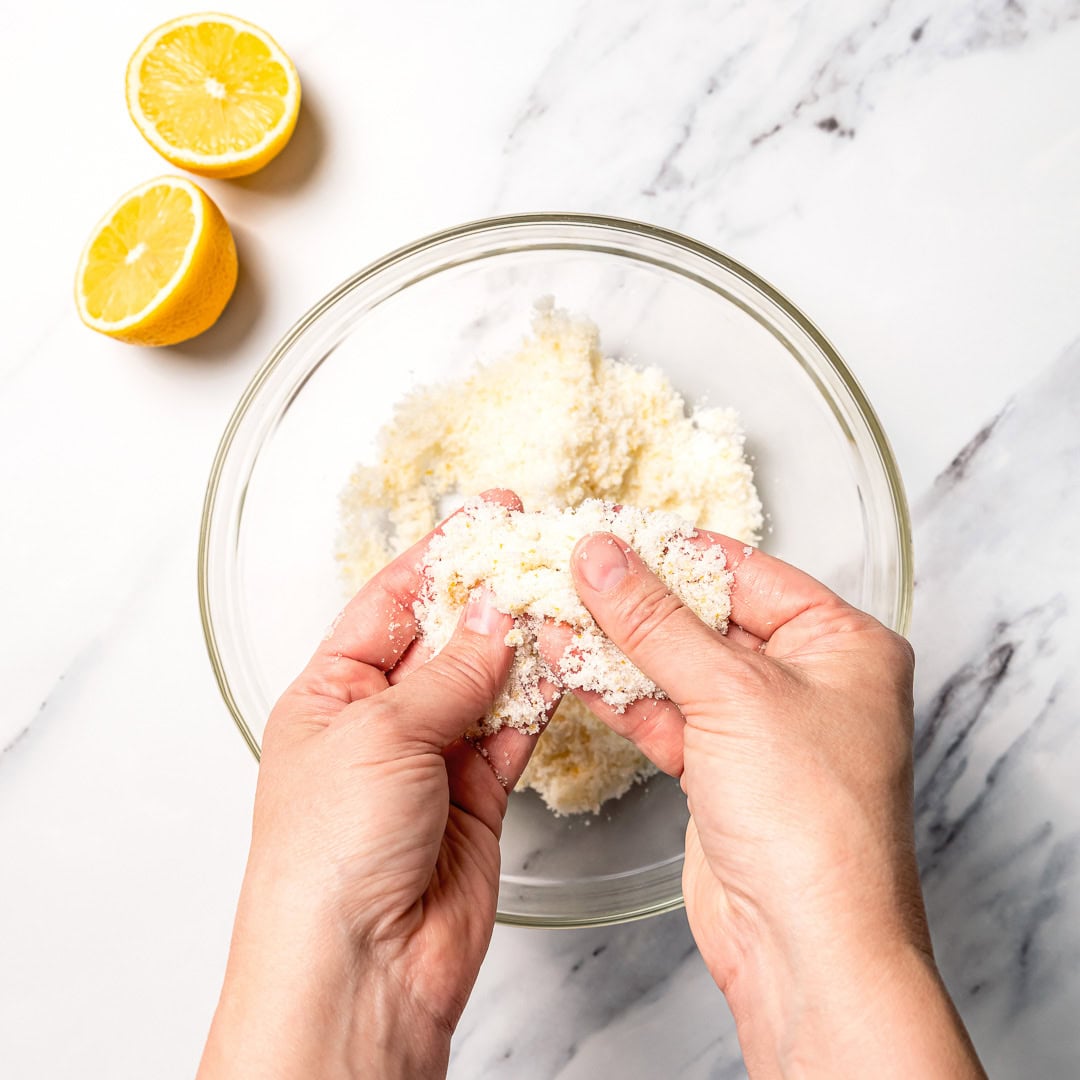 Hands rubbing sugar and lemon zest over bowl.