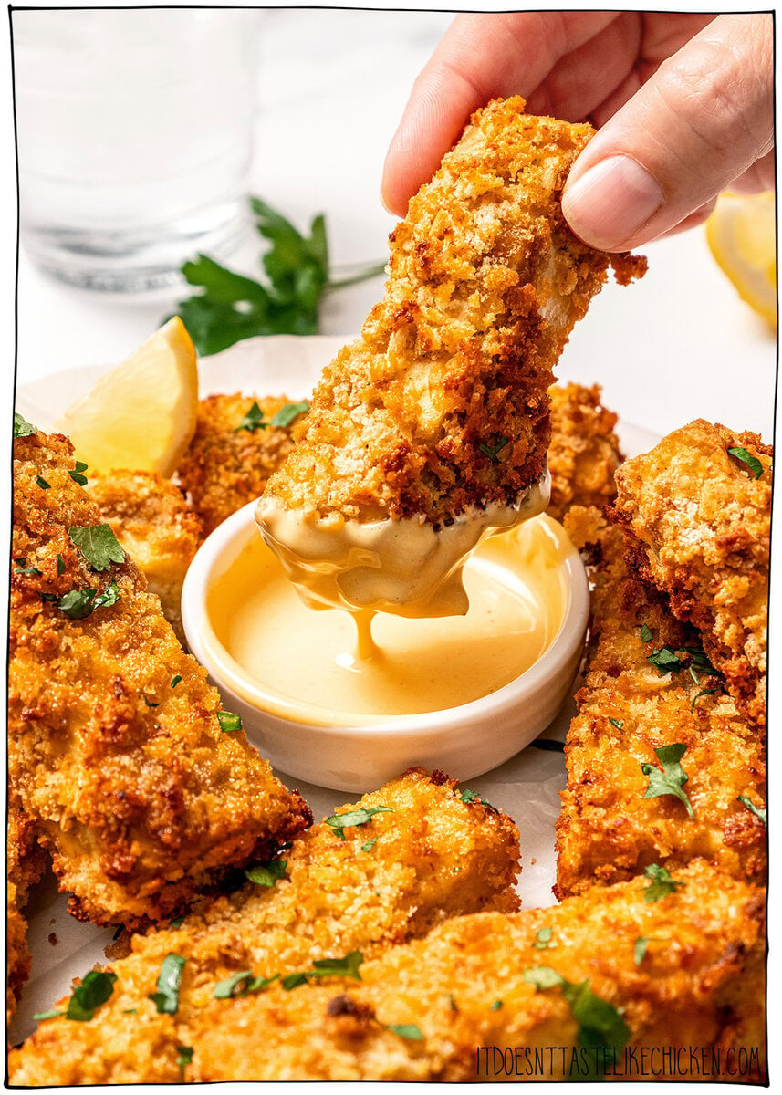 Plate of tofu chicken with sauce, with text overlay that reads vegan chicken fingers. Dipping tofu chicken finger into mustard sauce.