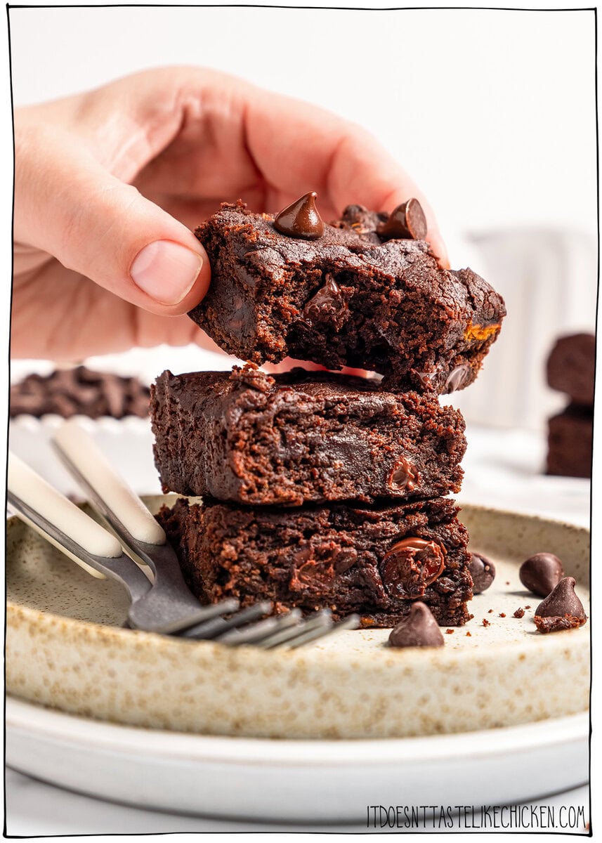 These vegan Sweet Potato Brownies are rich, fudgy, and loaded with deep chocolate flavor. You'd never know they're made with sweet potatoes! Hand placing sweet potato brownie with bite taken out of corner onto brownie stack on plate.