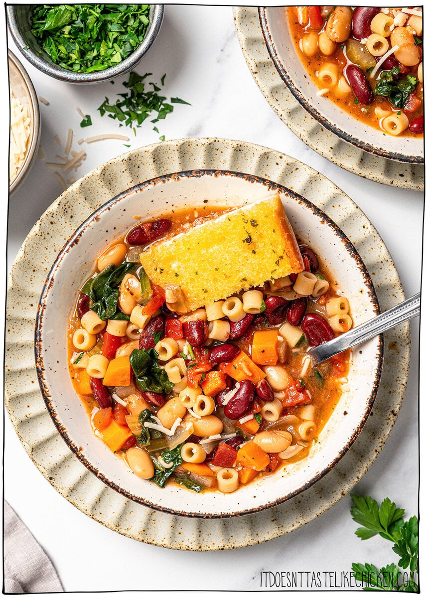 This vegan pasta e fagioli soup is hearty, cozy, and loaded with beans, pasta, and vegetables in a rich tomato broth. A budget-friendly meal! Bowl of vegan pasta e fagioli with slice of garlic bread.