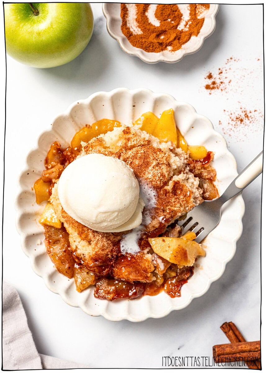 This Easy Vegan Apple Cobbler pairs tender spiced apples with a soft, buttery cake-like topping swirled with cinnamon sugar. So delicious! Bowl of vegan apple cobbler topped with scoop of ice cream.