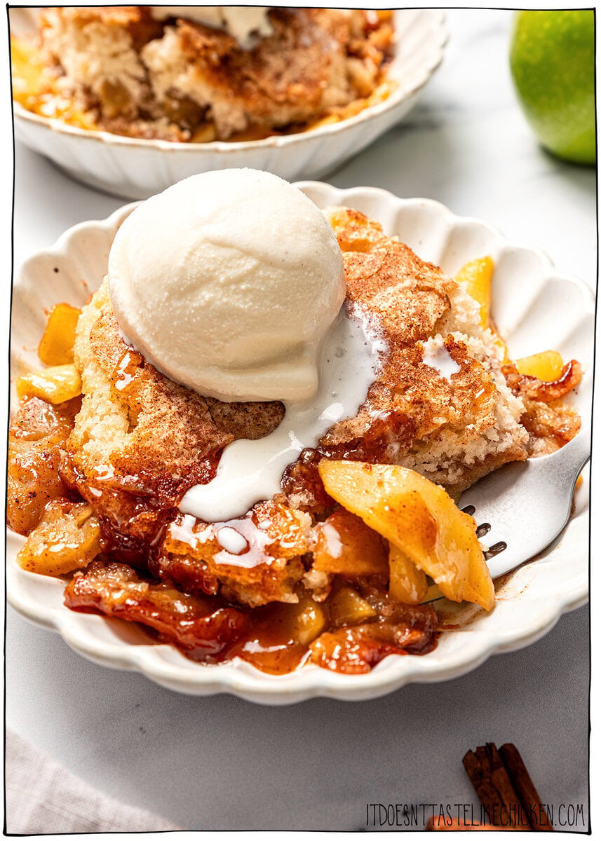 This Easy Vegan Apple Cobbler pairs tender spiced apples with a soft, buttery cake-like topping swirled with cinnamon sugar. So delicious! Vegan apple cobbler in bowl with scoop of ice cream.