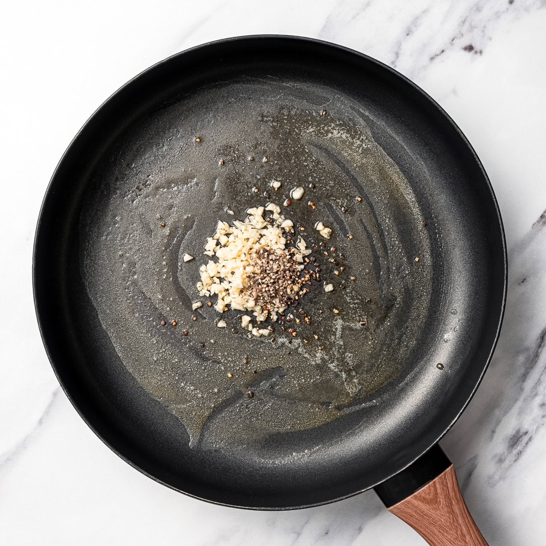 Cacio e pepe butter beans are creamy, peppery, and packed with buttery beans in a cheesy vegan sauce inspired by the classic Italian pasta! Garlic and black pepper in skillet.