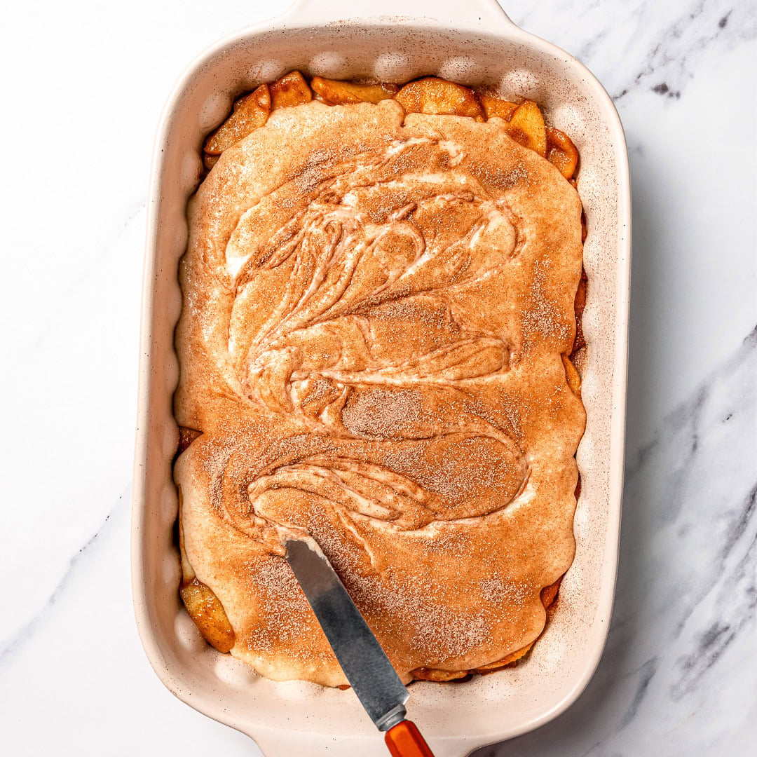 This Easy Vegan Apple Cobbler pairs tender spiced apples with a soft, buttery cake-like topping swirled with cinnamon sugar. So delicious! Knife swirling cinnamon into cobbler topping batter.