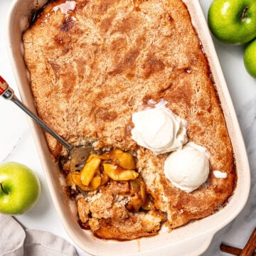 Spoon scooping serving of vegan apple cobbler from baking dish.