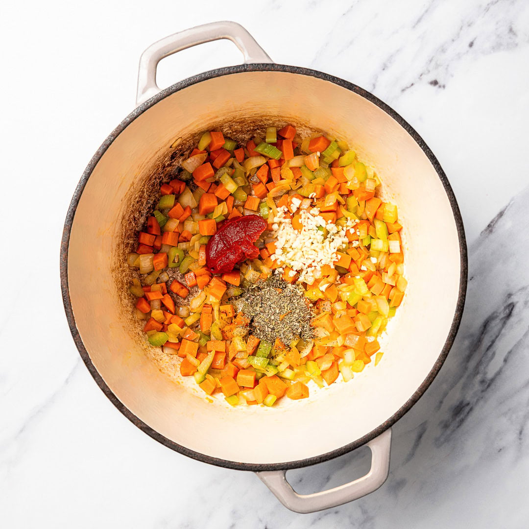 This vegan pasta e fagioli soup is hearty, cozy, and loaded with beans, pasta, and vegetables in a rich tomato broth. A budget-friendly meal! Garlic, Italian seasoning, and tomato paste added to pot of softened mirepoix.