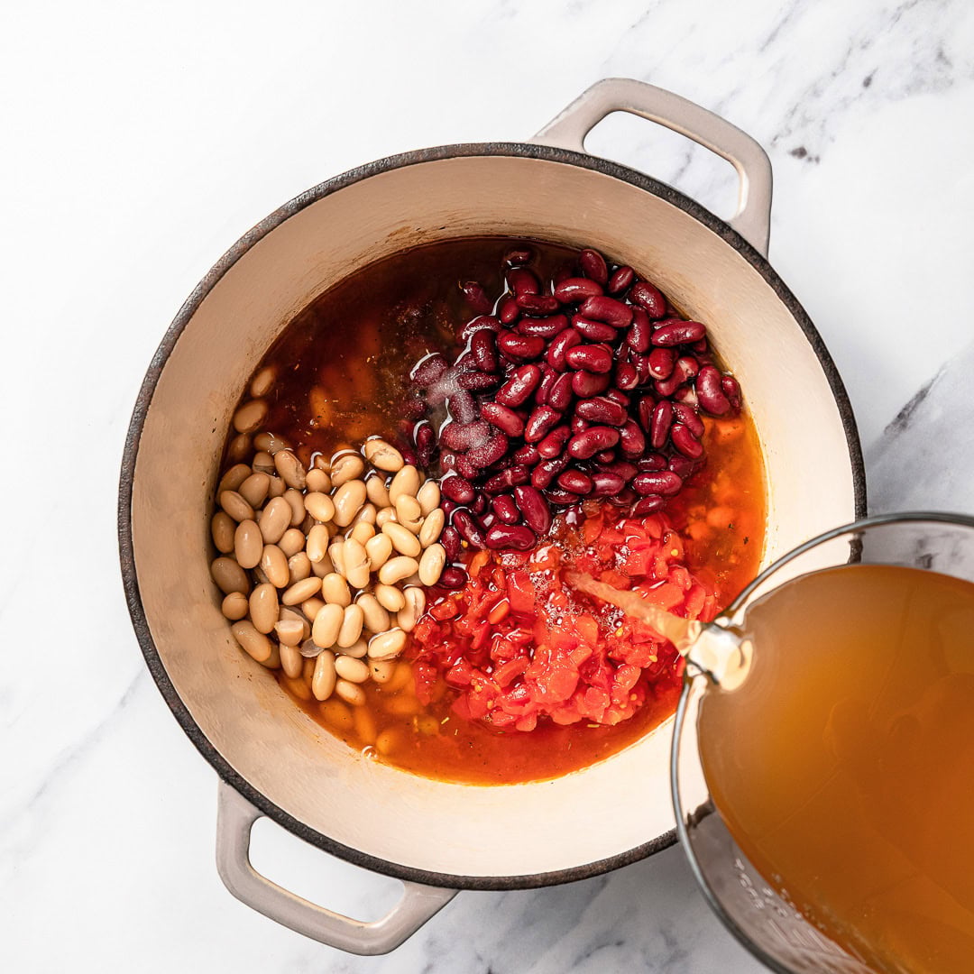 This vegan pasta e fagioli soup is hearty, cozy, and loaded with beans, pasta, and vegetables in a rich tomato broth. A budget-friendly meal! Pouring broth into pot of pasta e fagioli.