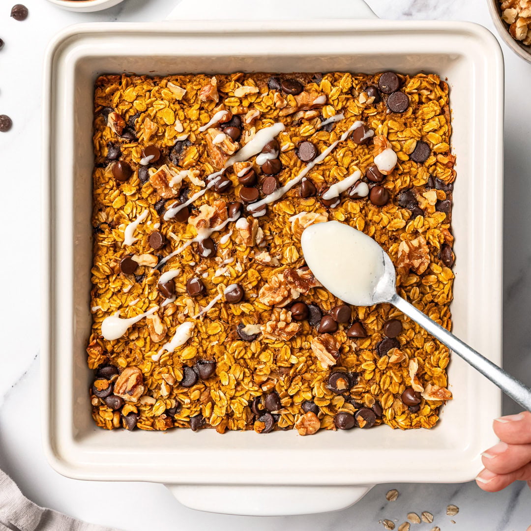 Drizzling cream cheese glaze onto chocolate chip pumpkin baked oatmeal.