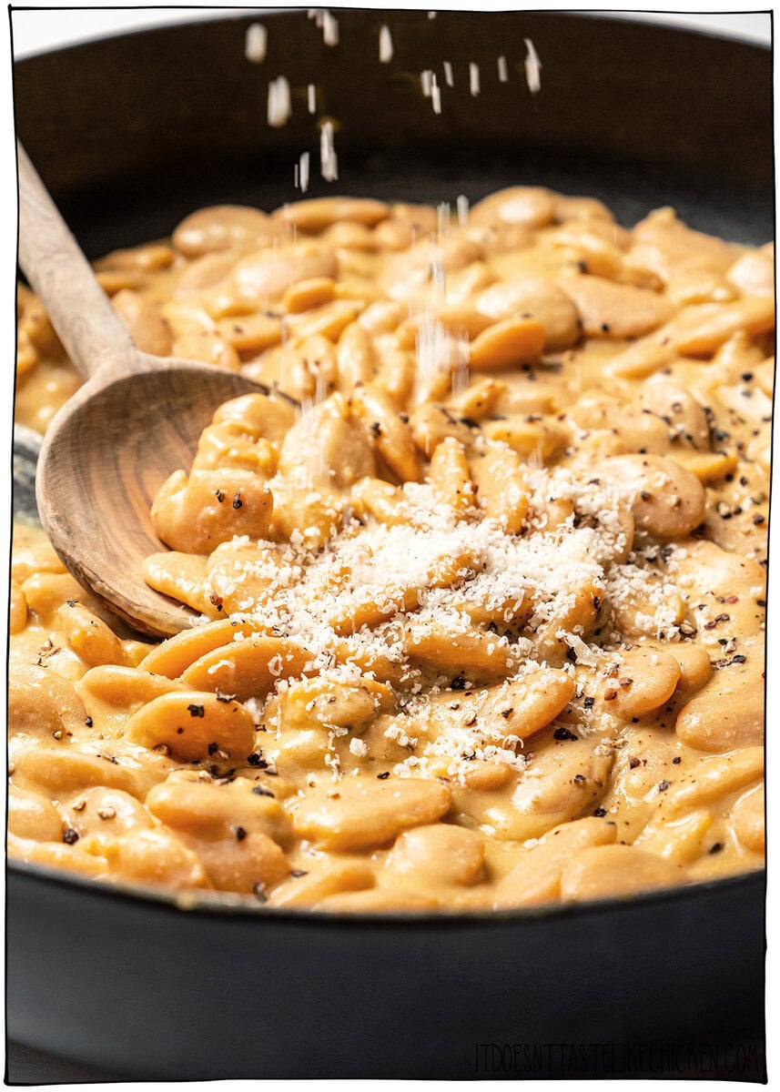 Cacio e pepe butter beans are creamy, peppery, and packed with buttery beans in a cheesy vegan sauce inspired by the classic Italian pasta! Vegan Parmesan being sprinkled into pot of cacio e pepe butter beans.