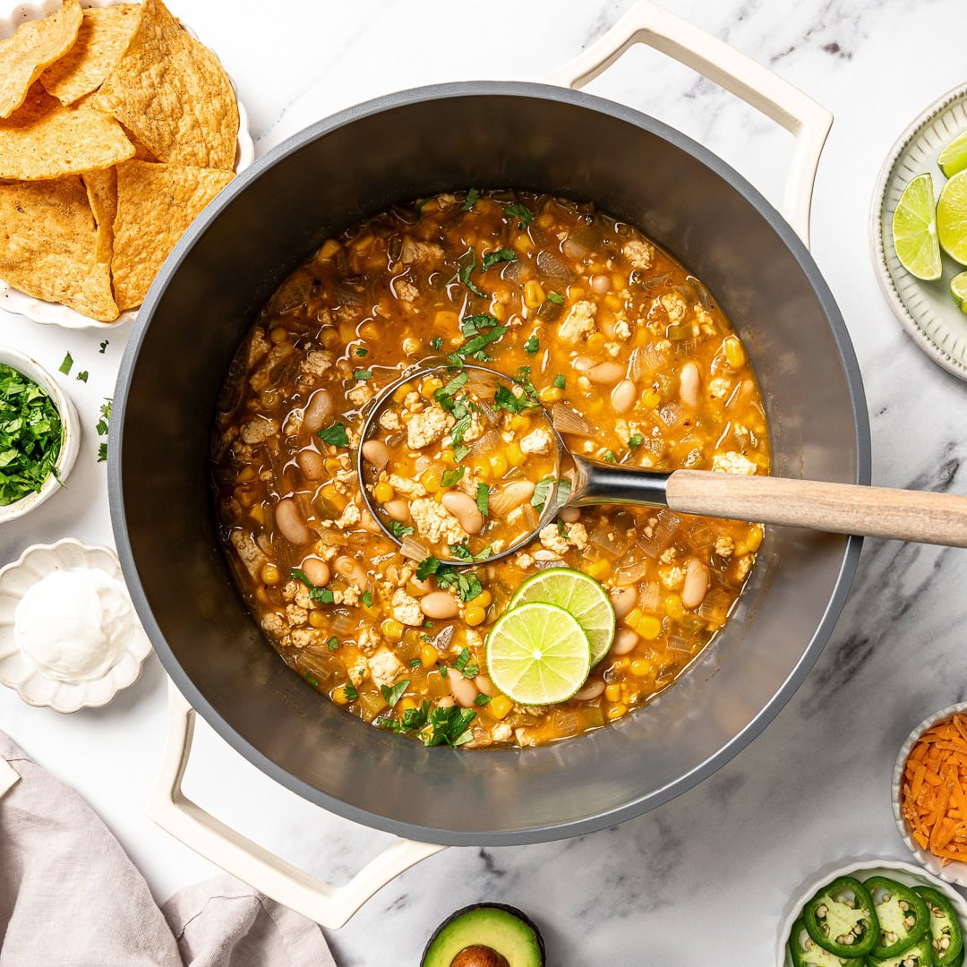 This easy Vegan White Bean Chili is creamy, hearty, and packed with cozy Southwestern-inspired flavors. Tofu adds a satisfying, meaty bite! Ladle of vegan white bean chili in pot with lime.